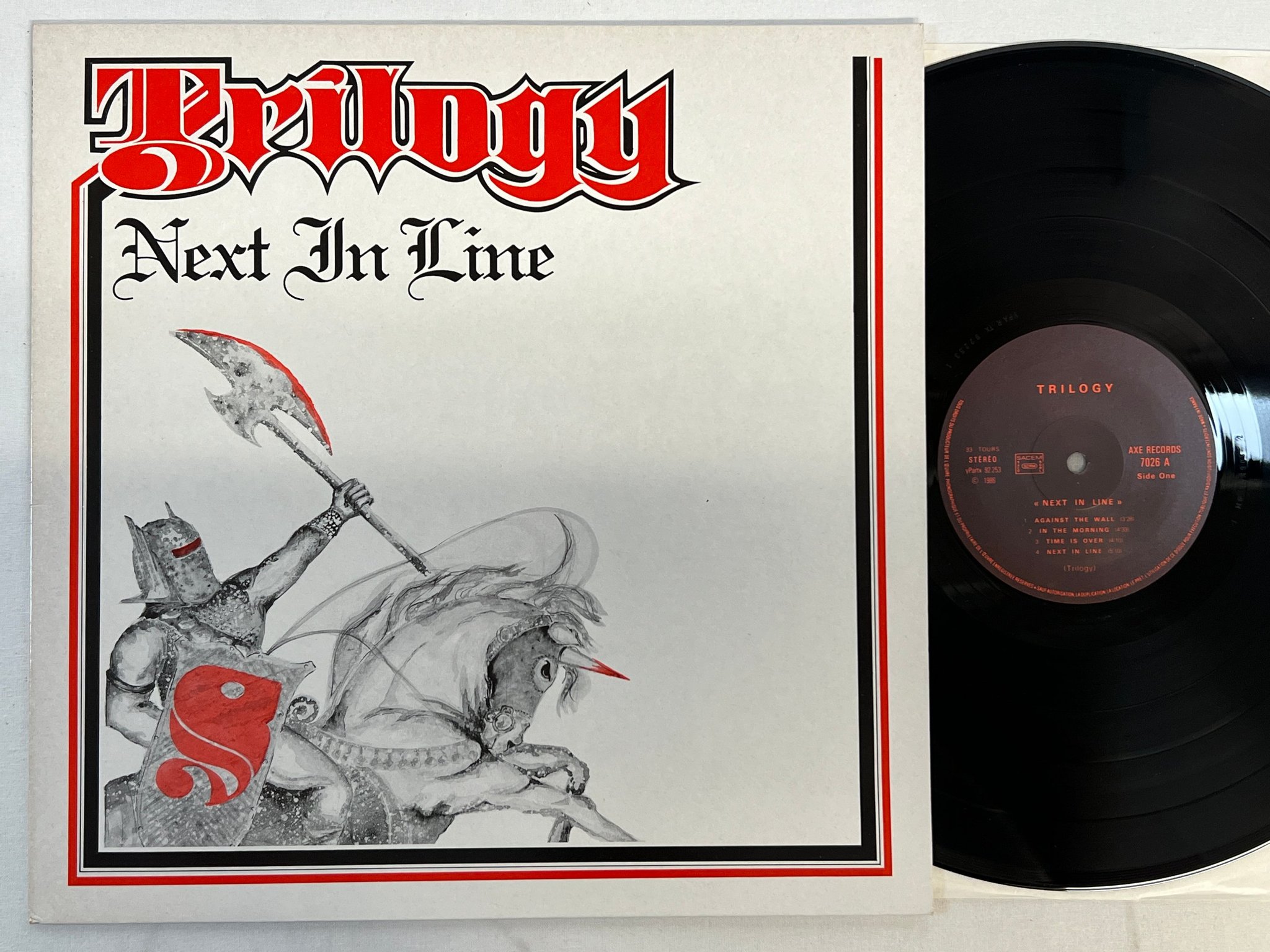 Omslagsbild för skivan TRILOGY next in time LP -86 Fra AXE 7026 ** VERY RARE HARD ROCK **