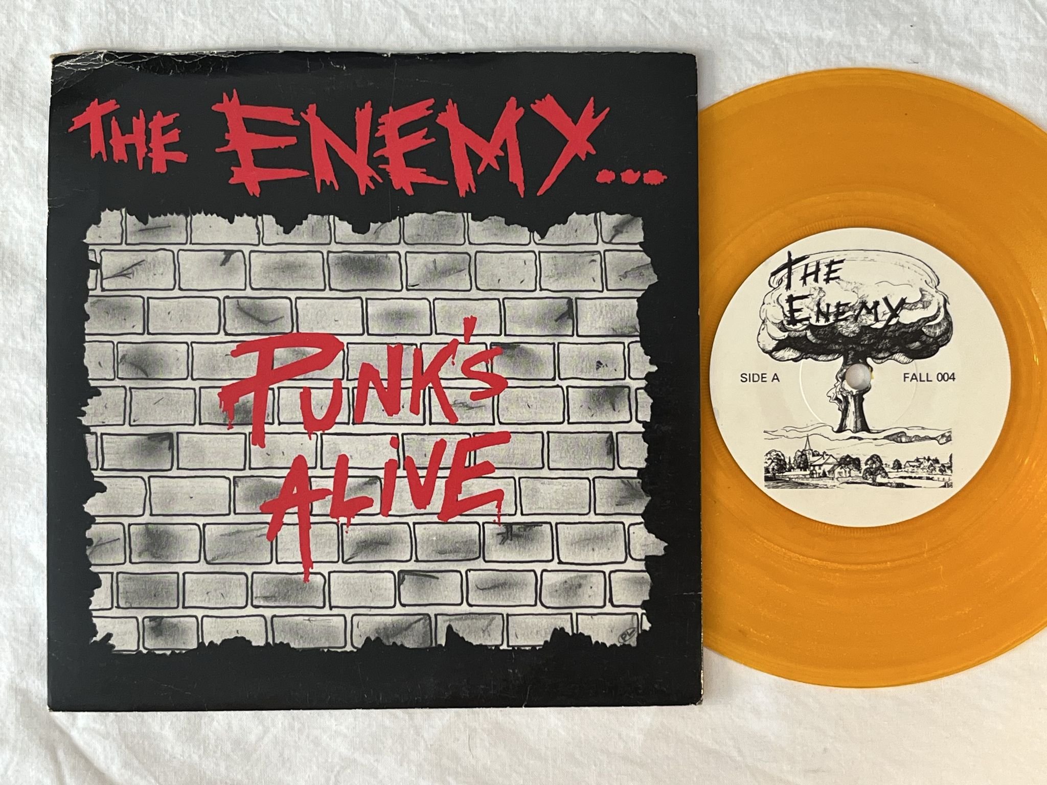 Omslagsbild för skivan THE ENEMY punk's alive 7" -82 UK FALLOUT RECORDS FALL 004 ** orange vinyl **